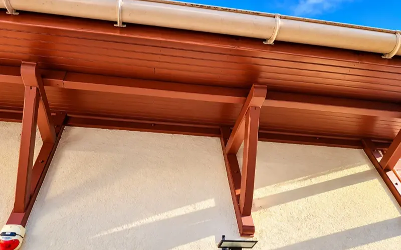 Avant-toit en bois verni et gouttière blanche le long de la façade